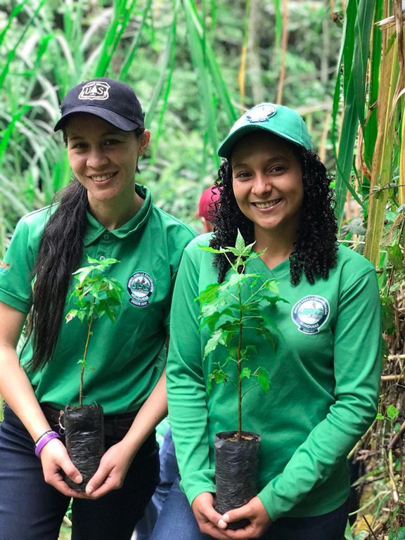Two girls in green shirts hold a tree sapling.