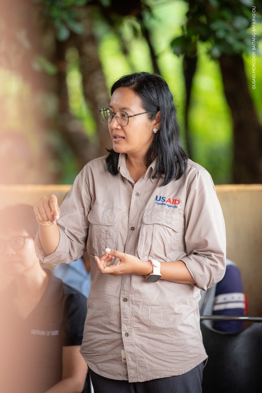 Woman in a tan shirt and glasses, gives instruction 