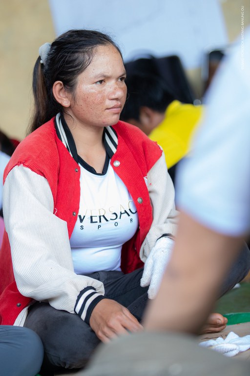 A woman in a red and white jacket sits on the ground. 