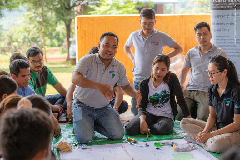 Several people sit on the floor, huddled around a map