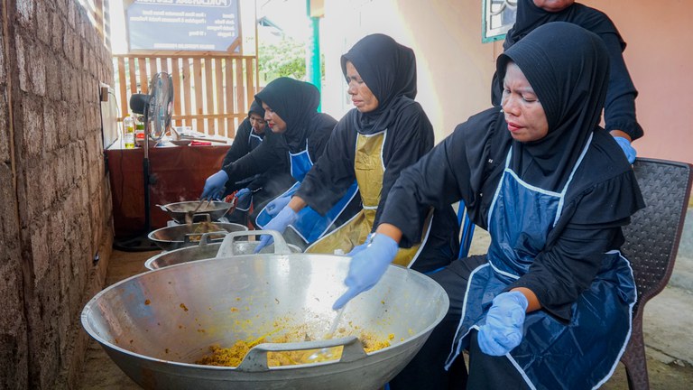 A group of women fish sellers and fishers in Indonesia cook in a big silver bowl