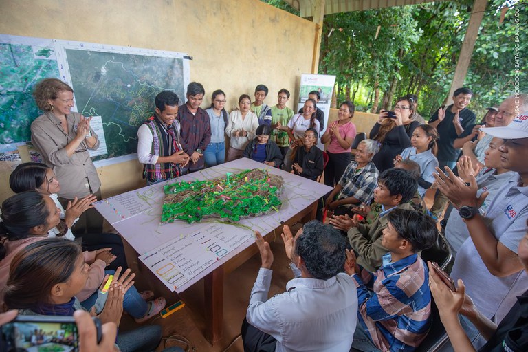 Group of people huddle around a 3D map clapping